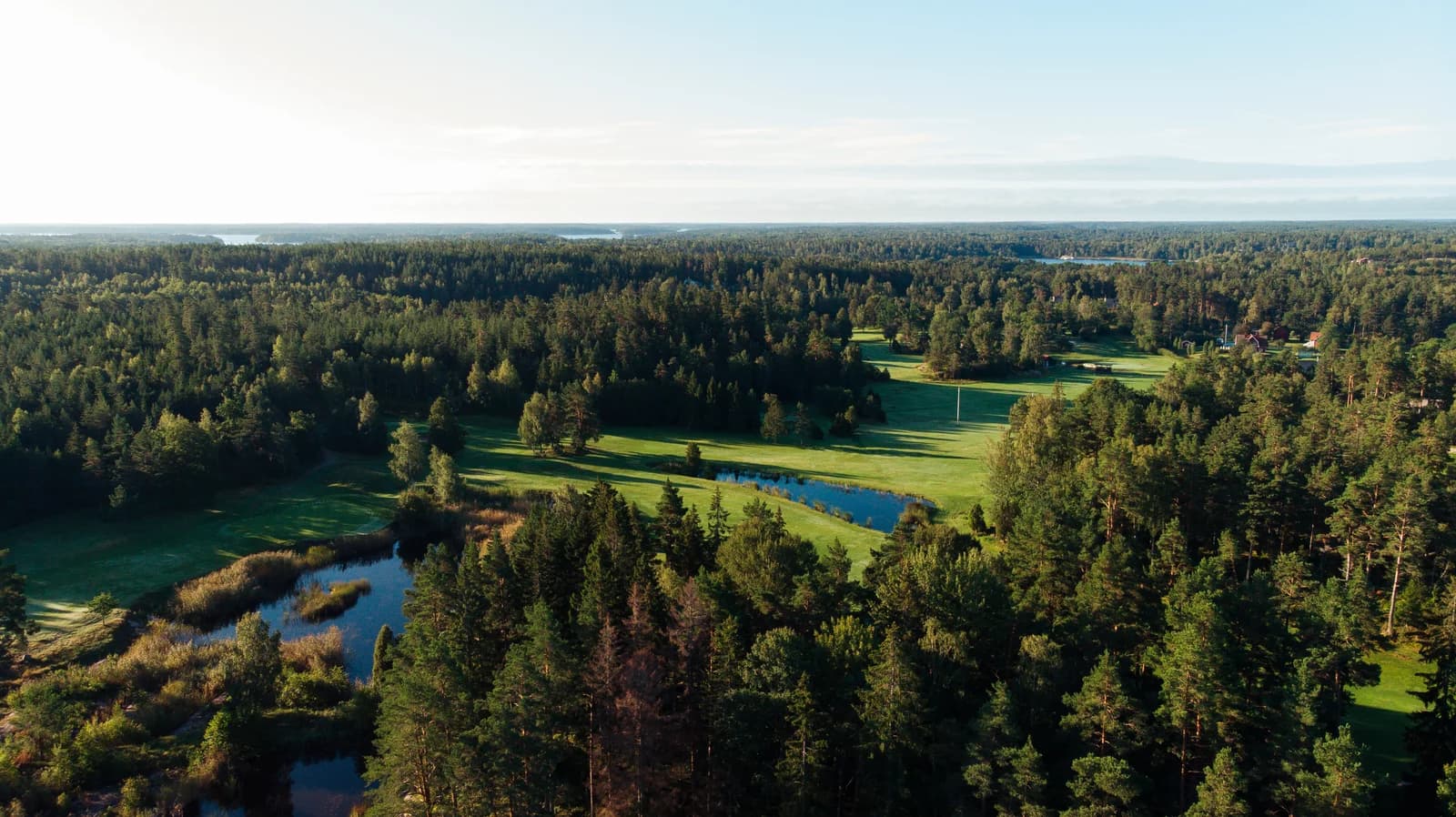 Flygvy över Ljusterö Golf med dammar, skog och skärgården i bakgrunden